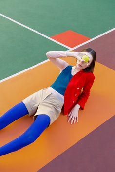 a woman laying on the ground with a tennis ball in her hand and an apple in her mouth