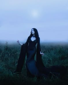 a woman with long black hair is standing in the middle of a grassy field at night