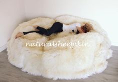 a woman laying on top of a fluffy white bean bag chair in a room with wood flooring