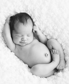 a black and white photo of a baby sleeping on top of a blanket with it's head resting on its hand