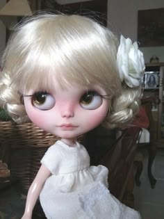 a doll with blonde hair wearing a white dress and flower in it's hair