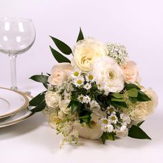 a bouquet of white and yellow flowers next to a wine glass on a table top