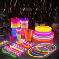 there are many neon colored cups and plates on the table with streamers around them