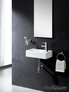 a white sink sitting next to a mirror on a black tiled wall in a bathroom