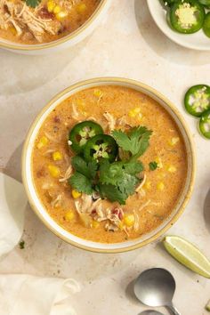 two bowls filled with soup and garnished with cilantro, limes, and green peppers