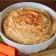 a white bowl filled with hummus next to carrots and crackers