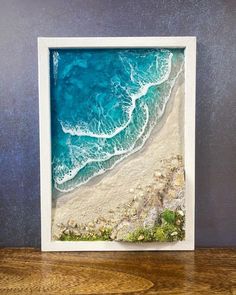 an aerial view of the ocean and beach in a white frame on top of a wooden table