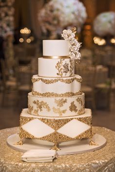 a white and gold wedding cake with flowers on the top is sitting on a table