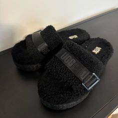 Ugg Fluffita Slide Black Black Slippers With Textured Footbed And Round Toe, Black Synthetic Slippers With Faux Fur Lining, Black Slippers With Faux Fur Lining, Black Winter Slippers With Round Toe, Black Slip-on Winter Slippers, Black Cushioned Slippers For Winter, Cozy Black Slip-on Slippers, Black Cozy Slippers With Round Toe, Black Comfy Slippers With Textured Footbed