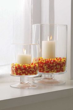 two clear vases filled with candy corn on top of a white counter next to a window