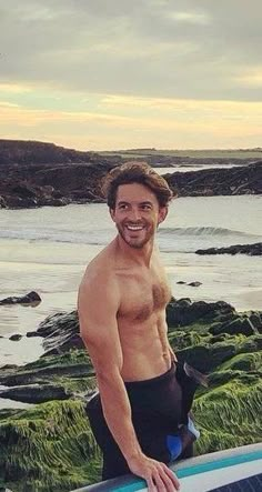 a shirtless man holding a surfboard near the ocean