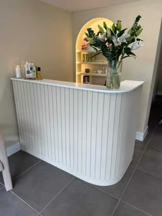 a white reception counter with flowers in a vase on the top and shelves behind it