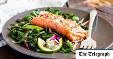 a plate with salmon, greens and lemon wedges on it next to a fork