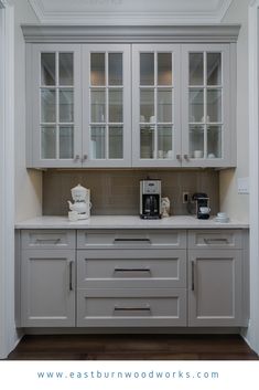 a kitchen with white cabinets and gray countertops is pictured in this image, there are two coffee makers on the left side of the cabinet