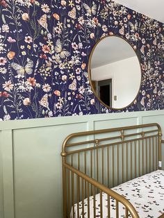 a baby crib in front of a wall with flowers on it and a mirror