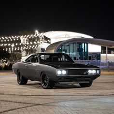 a black and gray car parked in front of a building at night with lights on