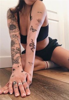 a woman sitting on the floor with tattoos on her arm and leg, both holding onto one hand