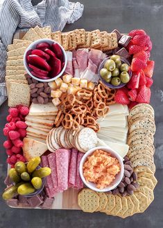 a platter filled with cheese, crackers, olives and meats on a wooden cutting board