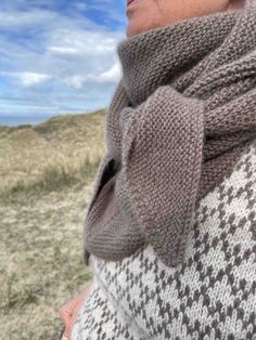 a woman wearing a sweater and scarf on top of a grass covered hill with blue skies in the background