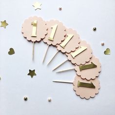 a table topped with lots of pink and gold cupcake toppers next to confetti