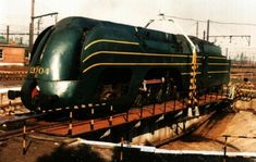 a green train is on the tracks in an industrial area with power lines above it