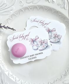 two baby shoes and a pink ball on a white plate with lavenders in the background