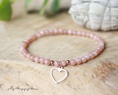 a pink beaded bracelet with a heart charm sits on top of a wooden table