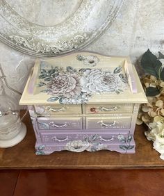 an old dresser has flowers painted on it and is next to a vase with flowers