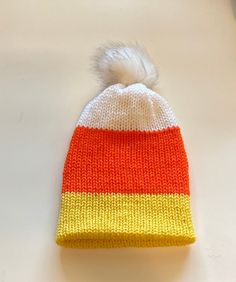 an orange and yellow knitted hat with a white pom - pom on top