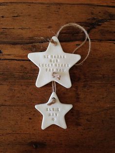 two white ceramic stars hanging from twine on wooden table with words written on them