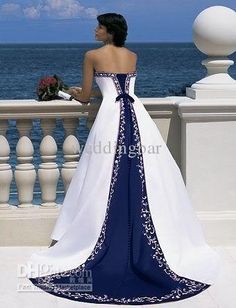 a woman in a white and blue wedding dress standing on a balcony overlooking the ocean