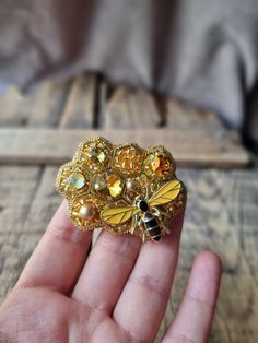 a hand holding a yellow and black bee brooch on it's left side