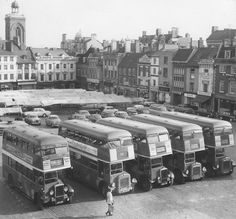 an old black and white photo of buses parked in a parking lot next to buildings