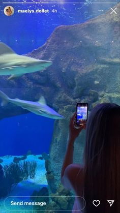 a woman taking a photo of some sharks in an aquarium with her cell phone screen