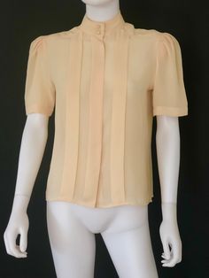 "Vintage circa 1970s retro short sleeved blouse from Ship 'N Shore, featuring front pleats, a hidden front button placket, a band collar with two self-covered buttons, and shirring at the sleeves tops. Semi-transparent. Fabric: 100% Polyester Approximate Measurements: Chest: 38\"; Shoulder: 17\"; Length: 22\" Labeled a Size 10 Condition: Retro blouse, circa 1970s, is in excellent vintage condition, as shown. Enjoy! *(International Buyers are welcome - however, please email me so I can check the Retro Blouse, Short Sleeved Blouse, Transparent Fabric, Formal Skirt, Retro Shorts, Soft Yellow, Vintage Elegant, Band Collar, Semi Transparent