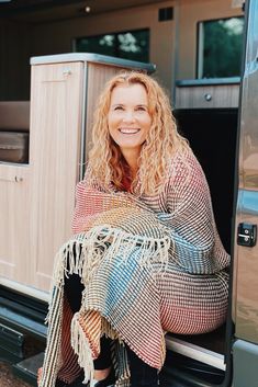 a woman sitting in the back of a truck with a blanket over her shoulders and smiling