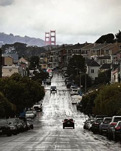 cars are parked on the street in front of some houses and a golden gate bridge