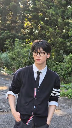 a young man wearing glasses and a black sweater is standing in front of some trees