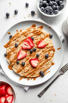 a white plate topped with oatmeal and strawberries next to bowls of blueberries