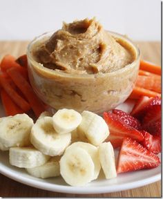 a white plate topped with bananas and strawberries next to a bowl of peanut butter