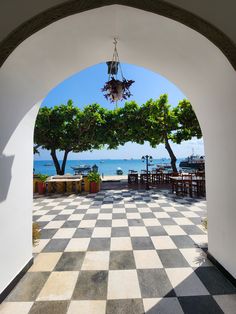 an archway leading to the beach with tables and chairs on it, along with trees