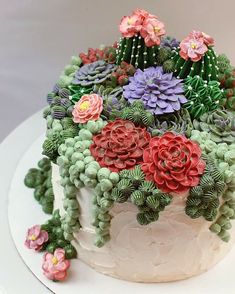 a cake decorated with flowers and succulents sits on a white platter