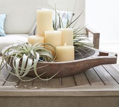 candles and air plants in a wooden bowl on a table with a couch behind it