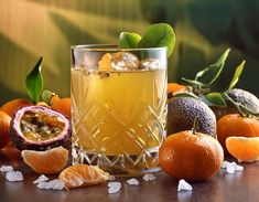 an orange drink with ice and fruit around it on a wooden table, surrounded by other citrus fruits