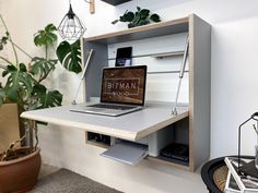 an open laptop computer sitting on top of a wooden shelf next to a potted plant