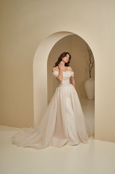 a woman in a white wedding dress posing for the camera with her hand on her shoulder