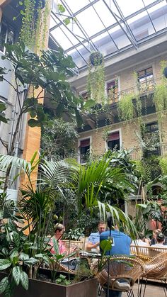 people are sitting at tables in the middle of a building with lots of greenery