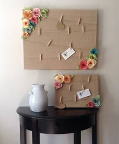 a table with a vase and two pieces of paper flowers on it next to a cork board