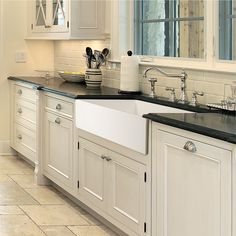 a kitchen with white cabinets and black counter tops is pictured in this image, there are utensils on top of the sink