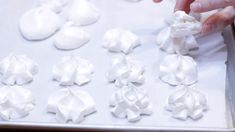 someone is decorating small white flowers with icing on a sheet of wax paper